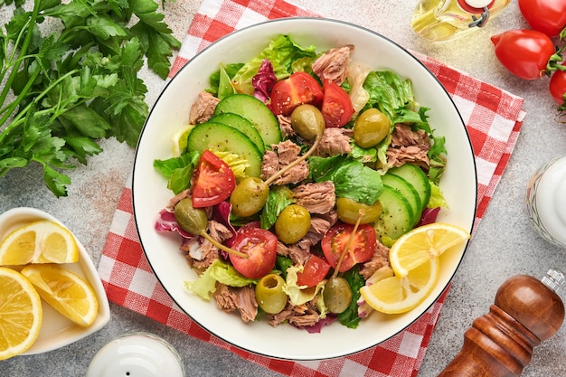 Salade de thon aux légumes frais, olives, câpres et citron servie dans un bol sur fond gris clair. Vue de dessus avec espace de copie.