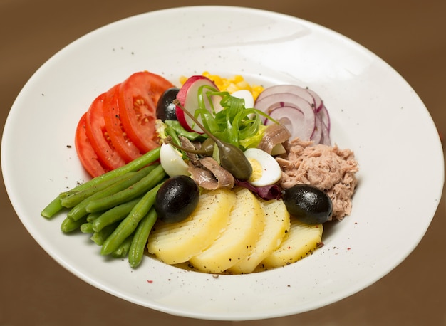 Photo salade de thon aux légumes, posée sur une assiette blanche, fond marron