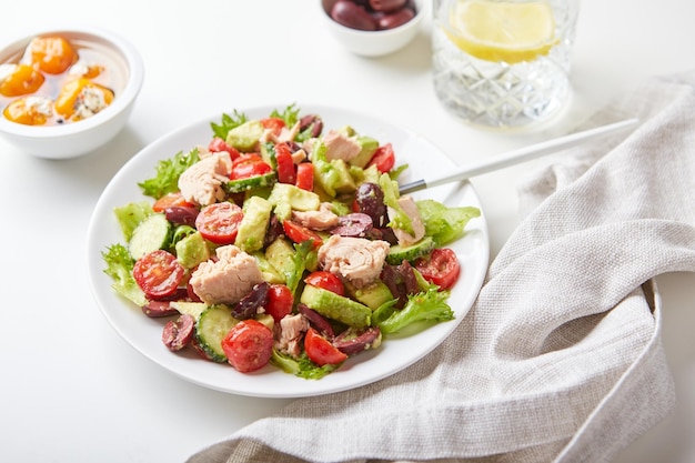 Salade de thon laitue concombres tomates olives et avocats en plaque blanche sur la table