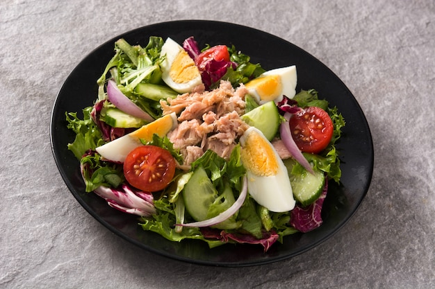 Salade de thon, oeuf et légumes sur plaque noire et surface grise
