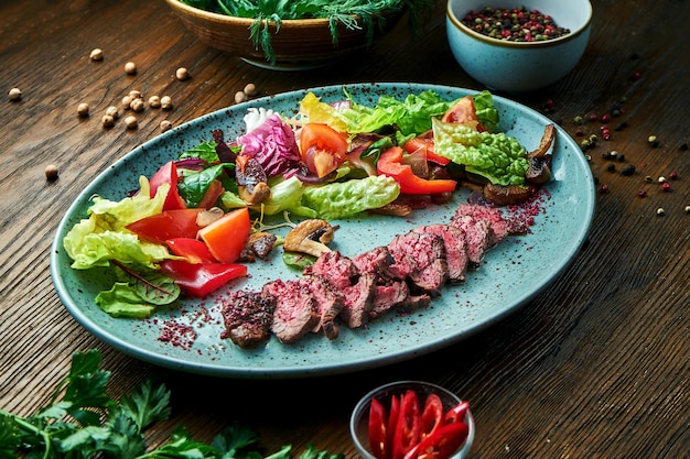 Salade tiède au boeuf saignant moyen et légumes frais, servie dans une assiette bleue sur une table en bois. Nourriture de restaurant. Gros plan, mise au point sélective