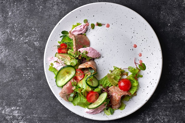 Salade tiède au veau et fromage à la crème, sur une assiette blanche et une table sombre