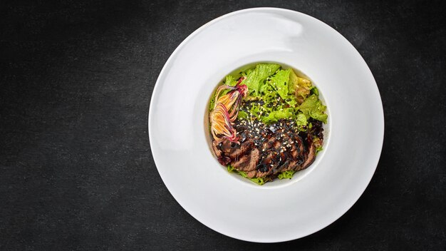 Salade tiède au veau haché sur une assiette sur fond sombre avec place pour texte