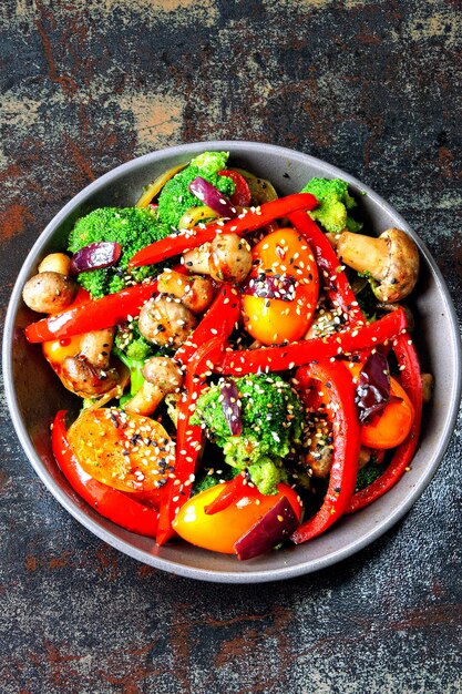 Salade tiède de brocoli, champignons et paprika rouge. Bol végétalien avec des légumes chauds sur un fond minable élégant. Nourriture saine. Déjeuner fitness aux champignons et légumes.