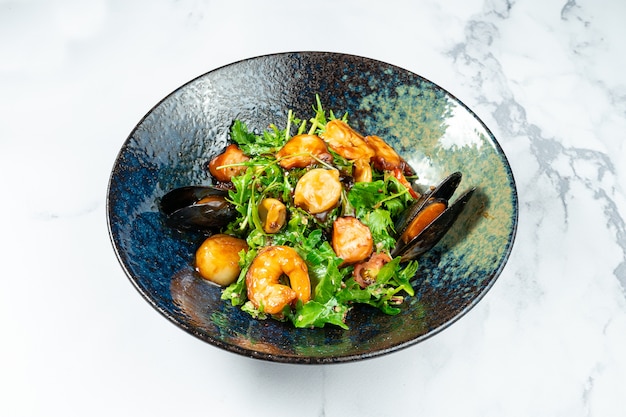 Salade tiède de fruits de mer dans un élégant bol noir sur une table en marbre. Salade de pétoncles. moules, crevettes en sauce aigre-douce. Aliments sains et équilibrés pour suivre un régime.