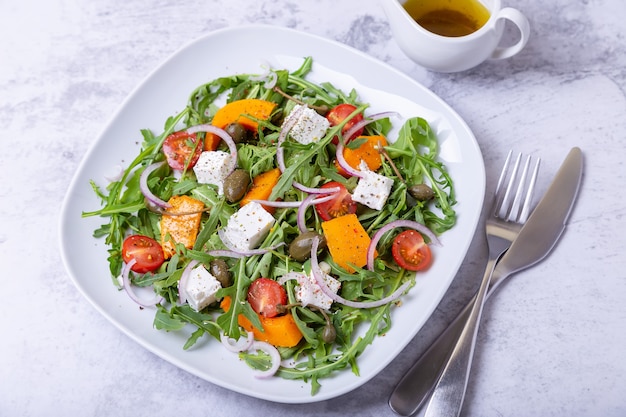 Salade tiède avec potiron, fromage feta, tomates, câpres, roquette et oignon rouge. Fermer.