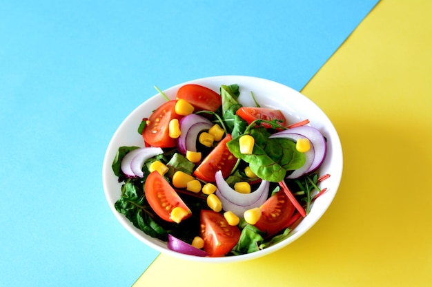salade avec tomate, oignon, maïs en conserve et salade verte dans un bol sur fond jaune et bleu