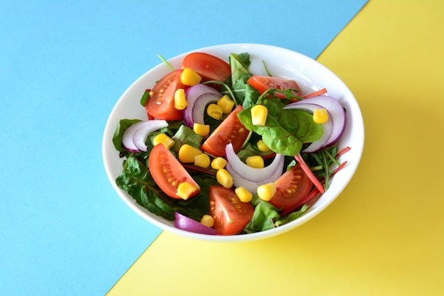 salade avec tomate, oignon rouge, maïs en conserve et rucola dans un bol blanc isolé