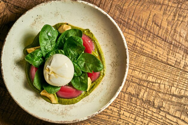 Salade de tomates burrata basilic et pesto dans une assiette sur un fond en bois