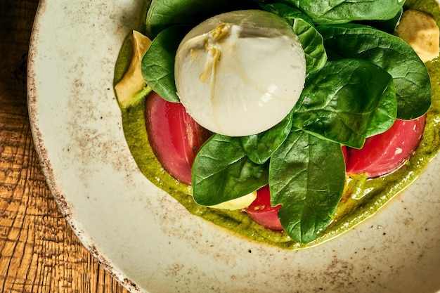 Salade de tomates burrata basilic et pesto dans une assiette sur un fond en bois