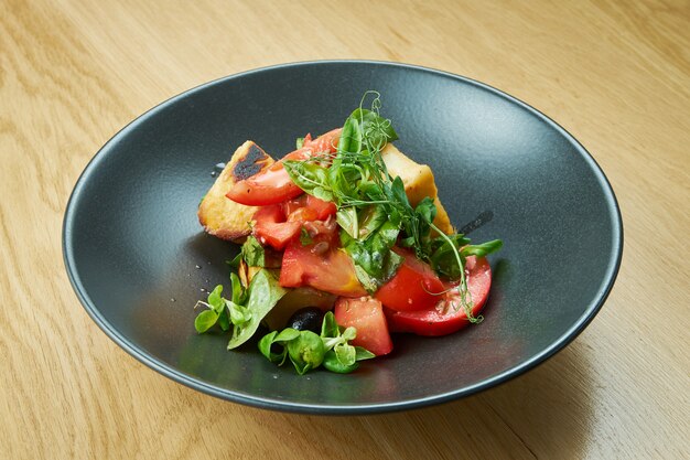 Salade de tomates cerises au fromage halumi frit et micro-vert dans un bol noir sur une table en bois. Nourriture de restaurant