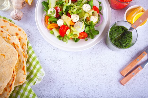 Salade de tomates cerises fraîches, mozzarella, basilic et autres légumes verts sur la table du dîner avec du pain plat pita