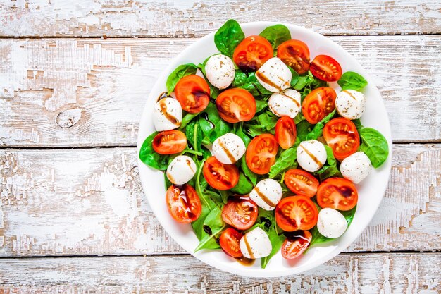 Salade de tomates cerises mozzarella et épinards avec sauce balsamique sur une table rustique blanche