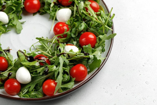 Salade de tomates cerises roquette et fromage mozzarella sur plaque ronde et fond gris