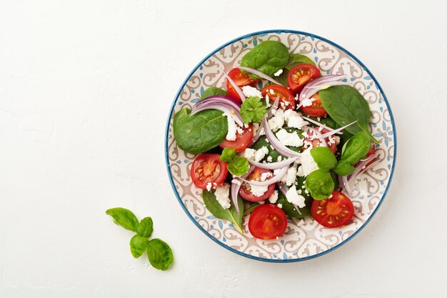 Salade de tomates, épinards, oignons rouges et fromage feta sur une assiette en céramique légère