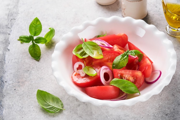 Salade de tomates fraîches avec des feuilles de basilic, de l'huile d'olive et de l'oignon dans un bol blanc sur fond clair Régime alimentaire traditionnel italien ou méditerranéen Vue de dessus