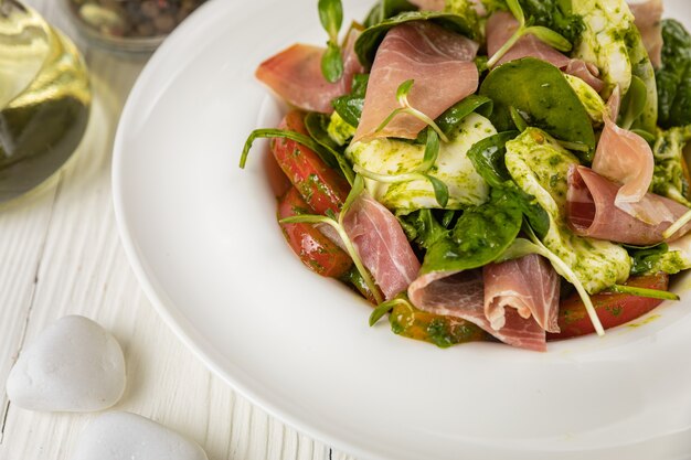 Salade de tomates mozzarella de Parme et de verdure Sur une assiette blanche et une table blanche