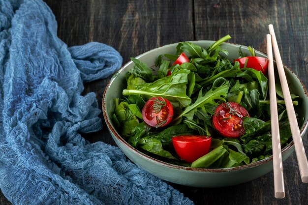 Salade de tomates, roquette et épinards sur une table en bois noir