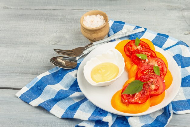 Salade de tomates végétaliennes avec des feuilles de basilic frais, des épices et une délicieuse sauce. Légumes rouges et oranges, mise en table. Fond en bois, espace de copie