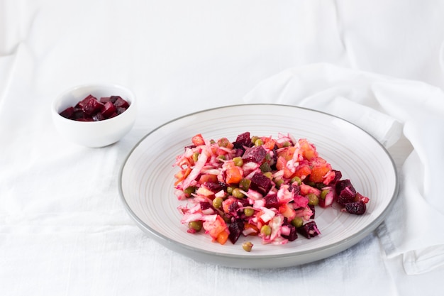 Salade traditionnelle russe aux légumes - vinaigrette sur une assiette et un bol de betteraves sur une table sur un chiffon