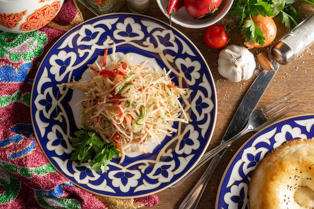 Salade végétalienne de légumes Orzu à base de chou blanc, tomates fraîches et concombres, assaisonnée d'huile d'ail dans une assiette avec un motif traditionnel ouzbek