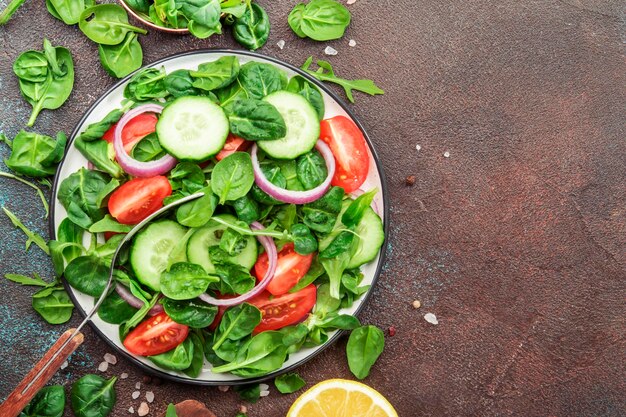 Salade végétalienne printanière aux épinards tomates cerises et oignons rouges Concept d'aliments sains Table en pierre brune Vue d'en haut Copier l'espace