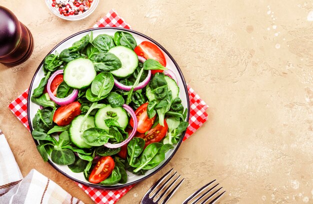 Salade végétalienne printanière aux épinards, tomates cerises, salade de maïs, bébés épinards et oignon rouge Concept d'alimentation saine Table en pierre beige Vue de dessus Espace de copie