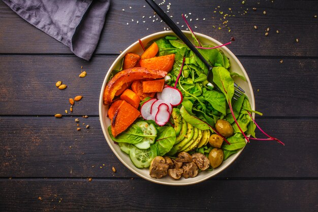 Salade végétalienne saine avec des légumes cuits au four, de l&#39;avocat et des olives dans un bol blanc sur du bois foncé