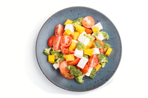 Salade végétarienne aux tomates brocoli feta et citrouille sur une plaque en céramique bleue isolé sur fond blanc