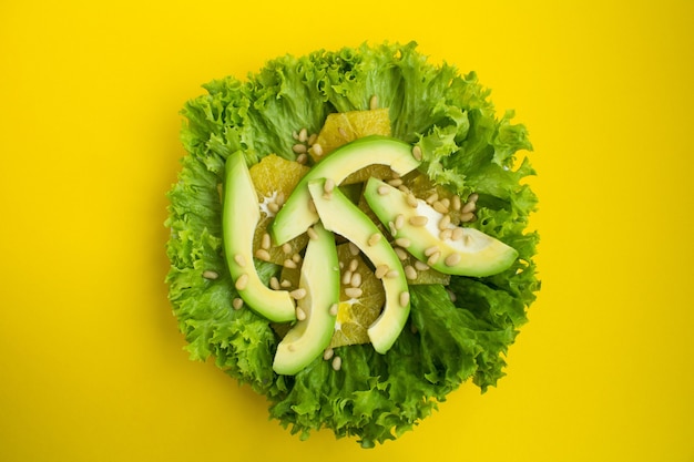 Salade végétarienne à l'avocat, feuilles de laitue, orange et pignons de pin sur fond jaune.Vue de dessus.