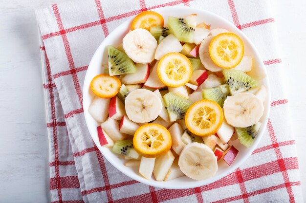 Salade végétarienne de bananes, pommes, poires, kumquats et kiwis sur une nappe en lin