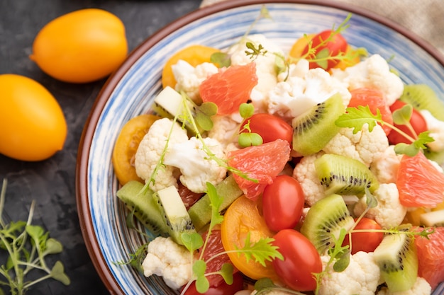 Salade végétarienne de chou-fleur chou, kiwi, tomates, pousses microgreen sur fond de béton noir