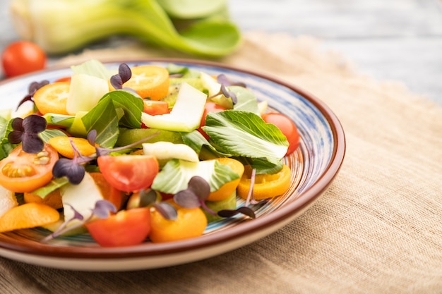 Salade végétarienne de chou pac choi, kiwi, tomates, kumquat, germes micro-verts sur une surface en bois gris. Vue latérale, mise au point sélective.