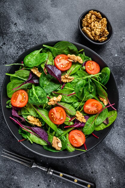 Salade végétarienne avec mélange de feuilles de mangold, bette à carde, épinards, roquette et noix dans un saladier. Fond noir. Vue de dessus.