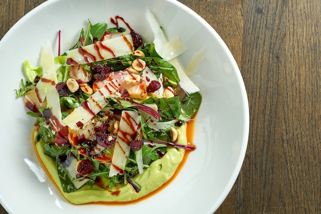 Salade végétarienne avec mousse d'avocat, parmesan, épinards, sauce aux baies et pommes au four dans une assiette sur une table en bois