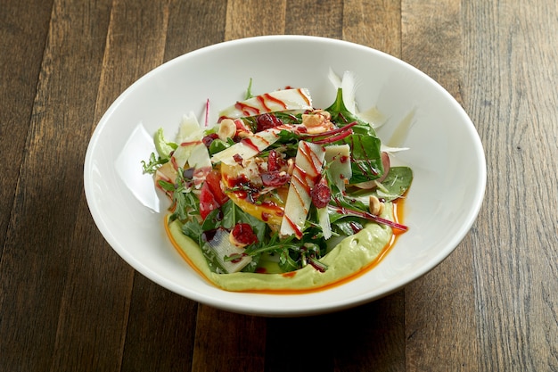 Salade végétarienne avec mousse d'avocat, parmesan, épinards, sauce aux baies et pommes au four dans une assiette sur une table en bois