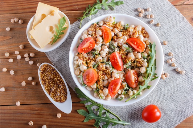 Salade Végétarienne De Pois Chiches Bouillis, Fromage, Roquette, Moutarde Et Tomates Cerises Sur Fond En Bois Marron.