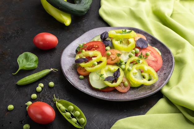 Salade végétarienne de pois verts, tomates, poivrons et basilic sur une surface de béton noir et textile vert