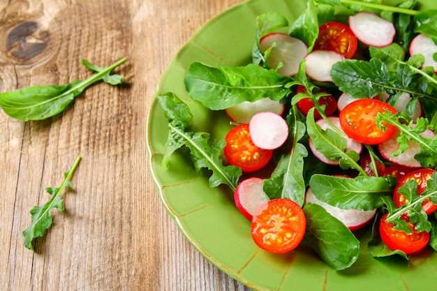 Salade végétarienne de roquette, tomate, radis et fromage mozzarella sur une vieille table en bois.