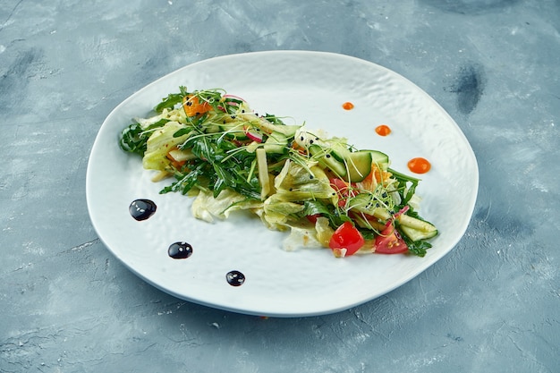 Salade végétarienne de style asiatique avec roquette, tomates, oranges et feuilles de laitue sur plaque blanche