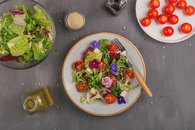 Salade végétarienne avec tomate, laitue et fromage garnie de fleurs comestibles et d'ingrédients sur une table grise. Concept de nourriture de printemps.