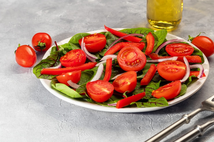 Photo salade végétarienne de tomates cerises, épinards, oignons rouges et poivrons avec du beurre. sur fond gris. copiez l'espace.