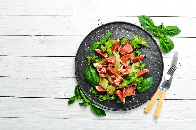 Salade verte avec concombre prosciutto et figue sur une assiette en pierre noire Nourriture Vue de dessus Espace libre pour votre texte