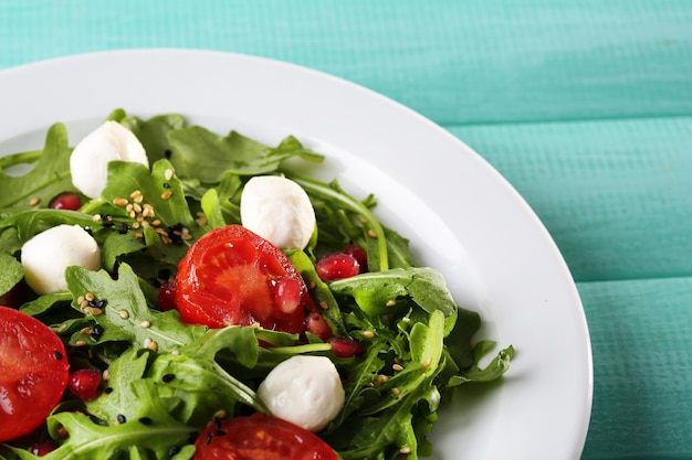 Salade verte faite avec des boules de mozzarella au fromage tomates roquette et sésame sur plaque sur fond de bois de couleur