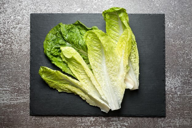 Salade verte fraîchement lavée sur une planche à découper en ardoise noire prête pour la cuisson. Ingrédients pour la cuisine, régime végétarien, alimentation saine.