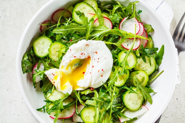 Salade verte avec œuf poché, concombre et radis dans un bol blanc. Concept d'aliments sains.