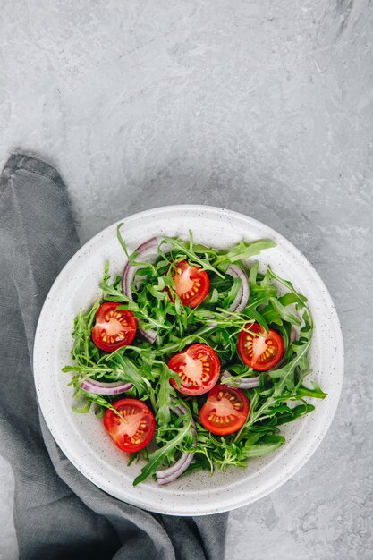 Salade verte roquette aux tomates et oignon rouge dans un bol Vue de dessus