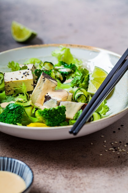 Salade verte vegan avec brocoli, tofu fumé et vinaigrette tahini dans un bol blanc,