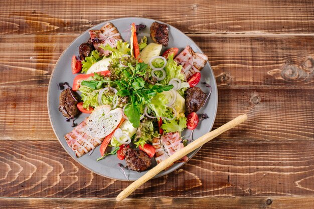 Une salade de viande grillée, bacon et légumes sur fond de bois