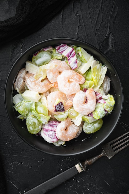 Salade Waldorf traditionnelle au céleri, ensemble de crevettes, avec sauce pomme et raisin, sur fond de pierre noire, vue de dessus à plat